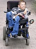 Zdjęcie przedstawia uśmiechniętego chłopaka na wózku inwalidzkim