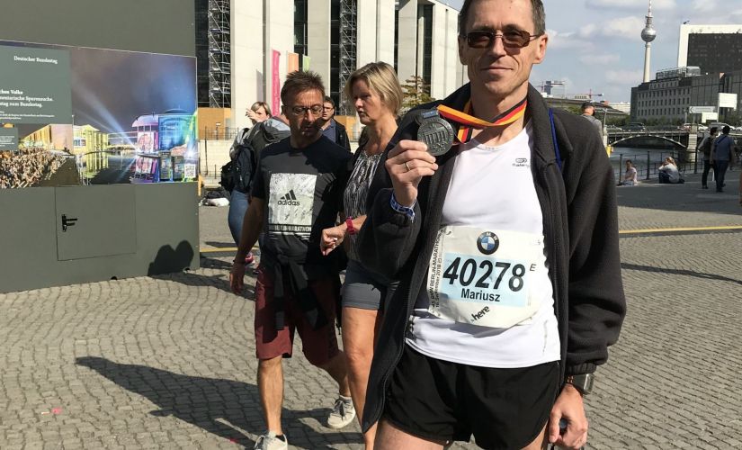 Prof. M. Wójcik stoi w stroju sportowym i prezentuje medal z maratonu w Berlinie z 2018 r.