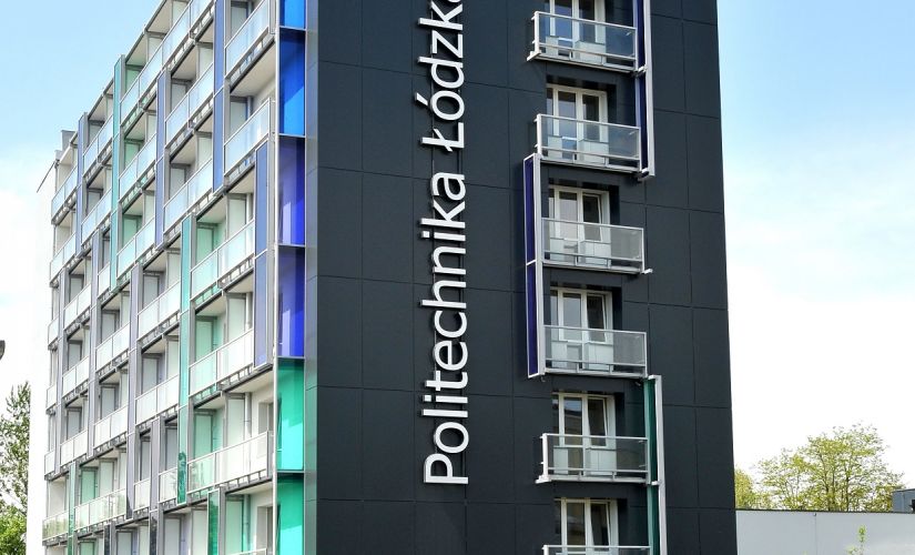 8 piętrowy budynek akademika uczelni. Ściana frontowa czarna z pionowym napisem Politechnika Łódzka. Ścianę boczną tworzą przeszklone balkony.