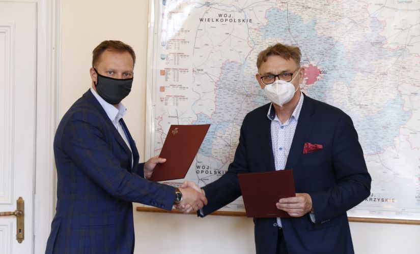 prof. Łukasz Kaczmarek (z lewej) i starosta pabianicki Krzysztof Habura ściskają sobie prawe dłonie. w lewych trzymają bordowe teczki z podpisanym porozumieniem.