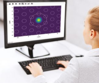 Ekran komputera na którym widać nierównomiernie rozłożone kółka na fioletowym tle. Widoczny także fragment kobiety w białym fartuchu pracującej na komputerze.