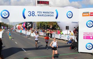 Meta: nad ulicą, którą biegną pojedynczy biegacze duży baner z napisem: 38. PZU Maraton Warszawski.