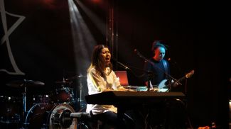 Eliza Tkacz on stage, at the piano during the concert. Guitarist in the background. 
