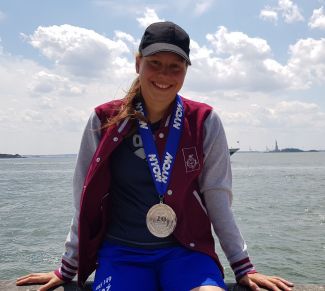 Ola Bednarek, studentka PŁ, siedzi na skraju łódki: na szyi ma duży srebrny medal. W tle woda.