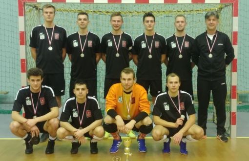 9-osobowa drużyna futsalu PŁ z trenerem S. Ścieszko stoją na tle bramki w dwóch rzędach.