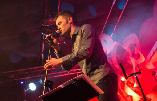 Maciek Rubacha śpiewa do mikrofonu podczas Festiwalu Piosenki Turystycznej YAPA 2020. W tle blask świateł.