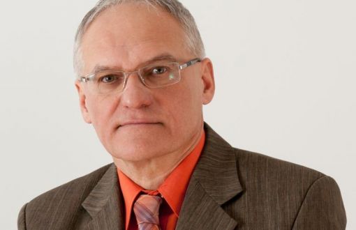 Zdjęcie portretowe: prof. Jan Awrejcewicz w szarym garniturze, łososiowej koszuli i krawacie na jasnej ścianie.
