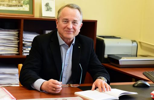 Zdjęcie portretowe: dr hab. inż. Jerzy Zgraja siedzi uśmiechnięty przy biurku w swoim gabinecie. W tle regał z dokumentami i urządzenia biurowe.