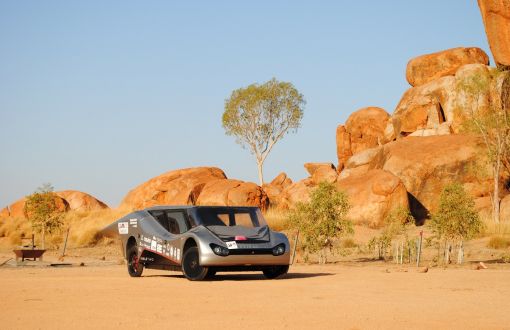 Srebrny Eagle Two - pojazd zespołu Lodz Solar Team, w australijskiej scenerii tj. na piasku, w tle skały o kolorze piasku.