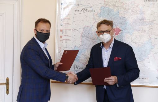 prof. Łukasz Kaczmarek (z lewej) i starosta pabianicki Krzysztof Habura ściskają sobie prawe dłonie. w lewych trzymają bordowe teczki z podpisanym porozumieniem.