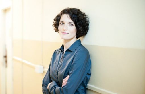 Zdjęcie portretowe: prof. Katarzyna Pernal stoi w niebieskiej koszuli na tle jasnej ściany.