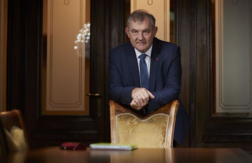 Rektor PŁ, prof. Krzysztof Jóźwik w garniturze, opiera o eleganckie krzesło. W tle przeszklone drzwi gabinetu.