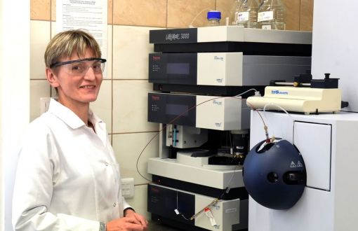 Prof. Beata Kolesińska w białym fartuchu i ochronnych okularach stoi przy stanowisku laboratoryjnym.