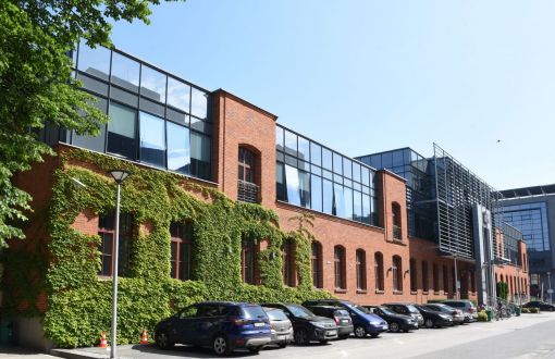 Fasada, nowoczesnego, dwukondygnacyjnego budynku Centrum Kształcenia Międzynarodowego: parter ceglany, częściowo porośnięty zielonymi pnączami, piętro całkowicie przeszklone, niebieskie.
