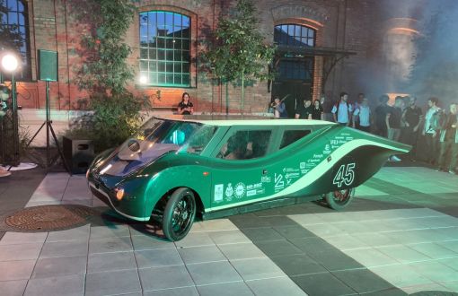 Eagle Two - elektryczny samochód zespołu Lodz Solar Team o nowoczesnym designie w kolorze zielonym na tle ceglanej zabudowy.