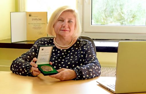 Zdjęcie portretowe: prof. Joanna Czaplińska-Kałużna siedzi przy biurku i prezentuje przyznanym jej Medalem im. Prof. Andrzeja Waksmundzkiego.